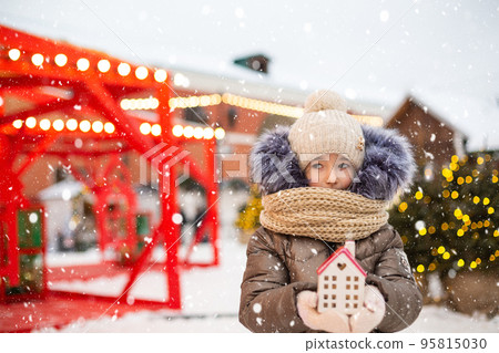 House, miniature cottage in hands of girl wearing mittens and warm clothes outdoor in snow. Family values, purchase housing, relocation, mortgage. Cozy home, Christmas, new year booking House, miniature cottage in hands of girl wearing mittens and warm clothes outdoor in snow. Family values, purchase housing, relocation, mortgage. Cozy home, Christmas, new year booking 95815030