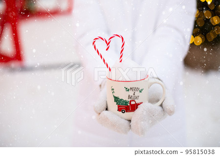 Woman with mug with snow, candy cane and inscription Merry and Bright in her hands outdoor in warm clothes in winter festive market. Fairy lights garlands decorated snow town for new year. Christmas Woman with mug with snow, candy cane and inscription Merry and Bright in her hands outdoor in warm clothes in winter festive market. Fairy lights garlands decorated snow town for new year. Christmas 95815038