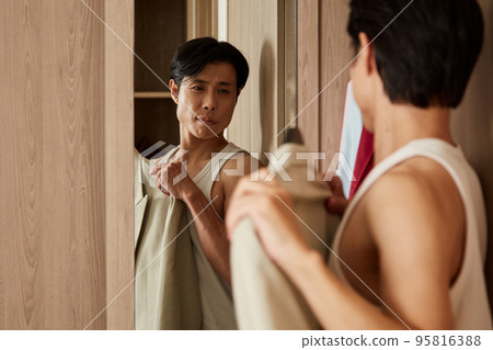 Asian young man looking at mirror when choosing suit to wear for business meeting 95816388
