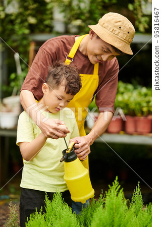 Smiling father teaching little son using garden sprayer for watering plants Smiling father teaching little son using garden sprayer for watering plants 95816467