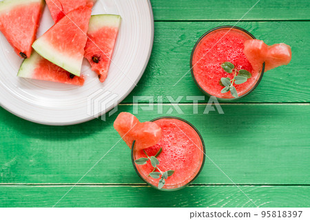 Fresh watermelon blended drink with mint leaves and a heart of watermelon in glasses and slices of watermelon on plate on a wooden table. Top view 95818397