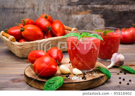 Ready-to-eat fresh tomato juice with basil leaves in glasses and tomatoes on a wooden table 95818402