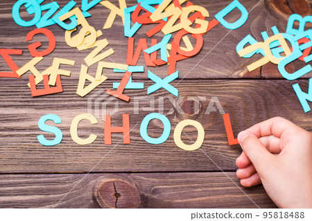 Children`s hands make up the word "school" from colored carved cardboard letters on a wooden background. Top view 95818488