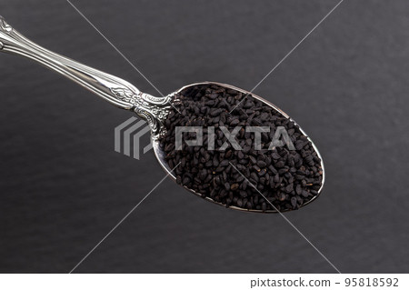 Black cumin seeds in a metal spoon over black background. Macro. Nigella. 95818592