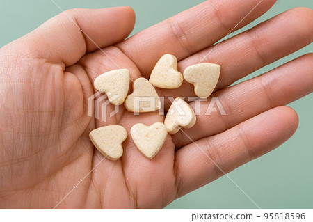 Pet vitamin pills on a woman hand palm. Heart shaped nutritional supplements for cats and dogs. 95818596