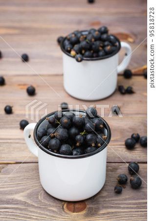 Ripe black currants in metal white mugs on a wooden table 95818728