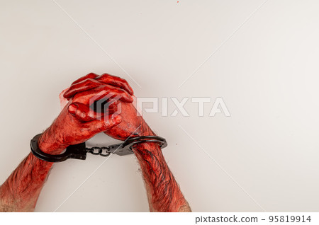 Bloodied male hands in handcuffs, folded on a white table. 95819914