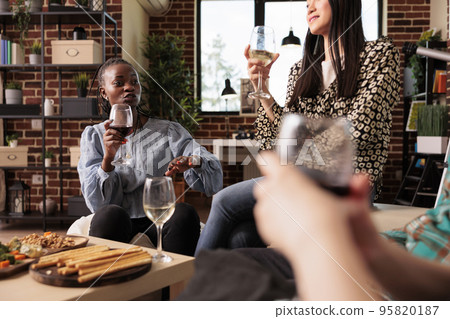 Different cultures female friends discussion, talking at coworkers house, apartment meeting. Diverse women group socializing, drinking wine, eating bread sticks at party. Different cultures female friends discussion, talking at coworkers house, apartment meeting. Diverse women group socializing, drinking wine, eating bread sticks at party. 95820187