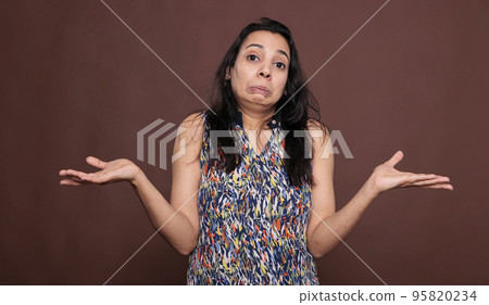 Confused indian woman shrugging shoulders with doubting facial expression, looking at camera. Puzzled lady standing with hands spread wide portrait, showing do not know gesture 95820234