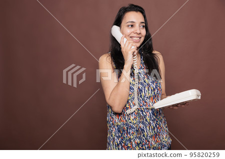Smiling indian woman talking on landline phone, customer support service. Cheerful lady chatting, holding retro telephone, person with positive facial expression answering call 95820259