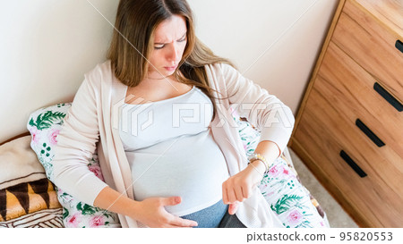 Pregnant contractions time. Pregnancy woman watching clock, holding baby belly. Childbirth time, contractions pain. Concept of pregnant, maternity, expectation for baby birth. Pregnant contractions time. Pregnancy woman watching clock, holding baby belly. Childbirth time, contractions pain. Concept of pregnant, maternity, expectation for baby birth. 95820553