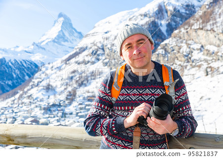 Positive man with camera standing on background of snowy Matterhorn peak 95821837