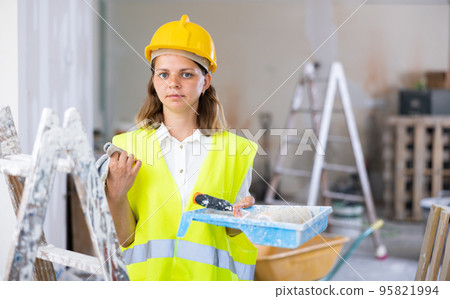 Woman builder holding paint roller and tray, home improvement works Woman builder holding paint roller and tray, home improvement works 95821994