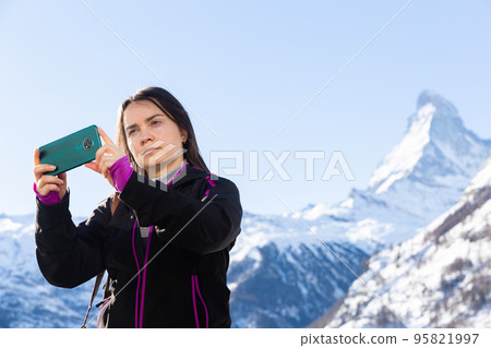 Woman recording video with phone while traveling in winter Swiss Alps 95821997
