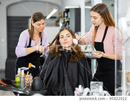 Make-up artist and a hairdresser serve a young female client 95822012
