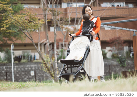mom holding baby and pushing stroller mom holding baby and pushing stroller 95823520