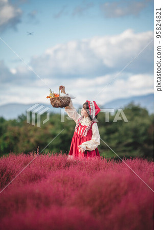A woman dressed as Little Red Riding Hood in a colorful flower garden A woman dressed as Little Red Riding Hood in a colorful flower garden 95824821