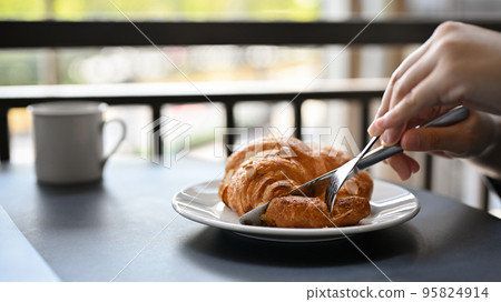 A female eating a delicious fresh French croissant for her breakfast at the coffee shop. A female eating a delicious fresh French croissant for her breakfast at the coffee shop. 95824914