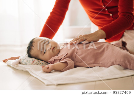 A baby lying on a towel and a mom sleeping together 95827409