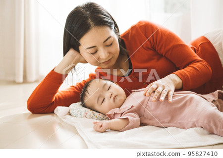 A baby lying on a towel and a mom sleeping together 95827410