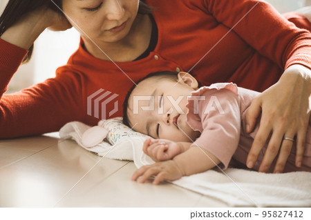 A baby lying on a towel and a mom sleeping together 95827412