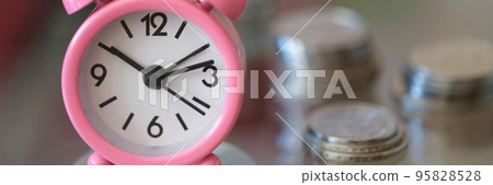 Pink alarm clock compass and stacks of coins closeup Pink alarm clock compass and stacks of coins closeup 95828528