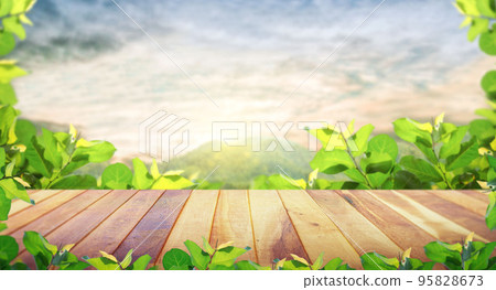 Brown blank wooden table top with spring green leaves with the mountain landscape. Brown blank wooden table top with spring green leaves with the mountain landscape. 95828673
