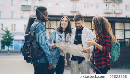 Young men and women with backpacks are looking at paper map standing in the street in foreign city and talking discussing journey. Navigation, youth and tourism concept. Young men and women with backpacks are looking at paper map standing in the street in foreign city and talking discussing journey. Navigation, youth and tourism concept. 95828868