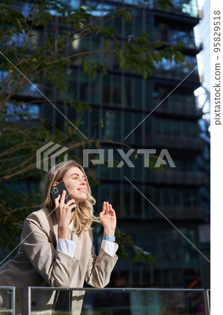 Vertical shot of businesswoman on a call, standing outside business center, talking on mobile phone 95829518