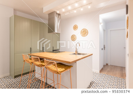Bright warm kitchen with appliances, wooden island and high chairs in modern apartment 95830374