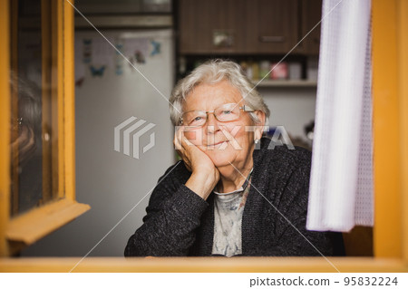 Lovely portrait of smilling grandmother by the window at a house Lovely portrait of smilling grandmother by the window at a house 95832224