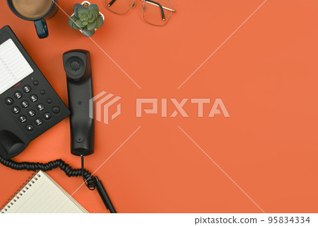 Above view of telephone, notepad, coffee up and eyeglasses on orange background. Flat lay, top view with copy space Above view of telephone, notepad, coffee up and eyeglasses on orange background. Flat lay, top view with copy space 95834334