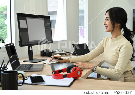 Attractive female photo editors sitting in creative workplace and retouching photos on personnel computer 95834337