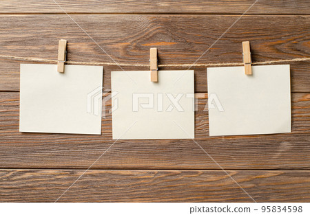 Empty paper sheets hang on a rope. A design element. Brown wooden background. Copy space. Empty paper sheets hang on a rope. A design element. Brown wooden background. Copy space. 95834598