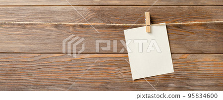 An empty piece of paper is hanging on a rope. A design element. Brown wooden background. Copy space. An empty piece of paper is hanging on a rope. A design element. Brown wooden background. Copy space. 95834600