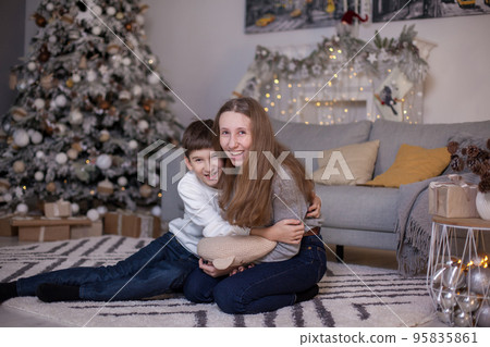 brother and sister sitting on floor near christmas tree 95835861