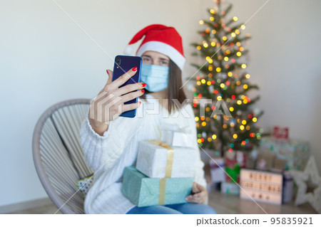 Woman in medical mask with gift boxes having a video call on phone 95835921