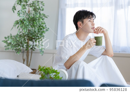 Young man sitting on bed and drinking drink 95836128