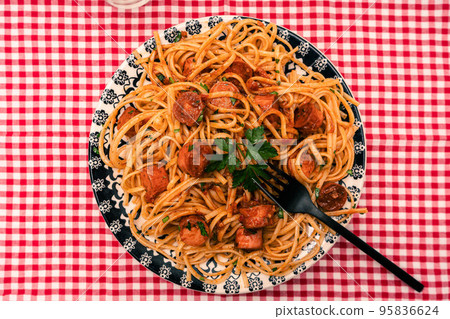 Hearty pasta dish with tomato sauce and sausage on a table with a red checkered tablecloth. Hearty pasta dish with tomato sauce and sausage on a table with a red checkered tablecloth. 95836624
