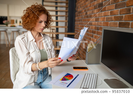 Female manager scrutinizing papers and looking involved Female manager scrutinizing papers and looking involved 95837010