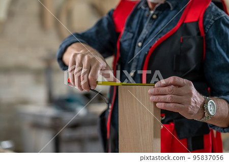 Carpenter making measurements with a measuring tape Carpenter making measurements with a measuring tape 95837056