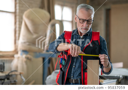 Carpenter making measurements with a measuring tape 95837059