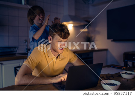 Dad working on a laptop while his son playing next to him 95837117