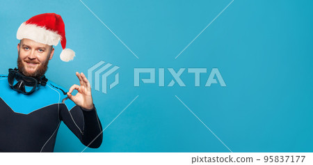 Happy man diver Santa showing okay sign and having fun on blue banner background Happy man diver Santa showing okay sign and having fun on blue banner background 95837177