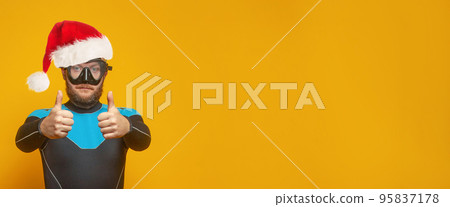 Handsome man diver man in Santa hat showing thumb up against yellow background Handsome man diver man in Santa hat showing thumb up against yellow background 95837178