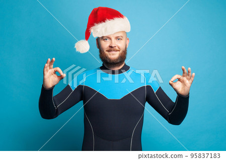 Christmas concept. Happy man diver in Santa cap holding okay sign standing on blue background Christmas concept. Happy man diver in Santa cap holding okay sign standing on blue background 95837183