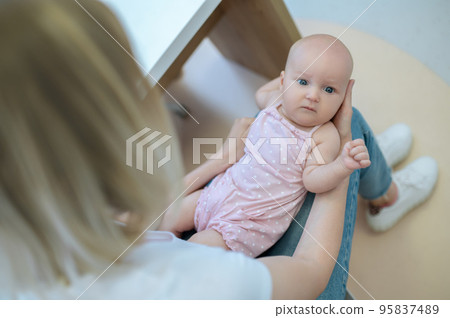 Blonde mom talking to a male pediatrician and holding her baby 95837489