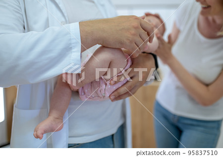 Male doctor holding a baby in hands before the medical check Male doctor holding a baby in hands before the medical check 95837510