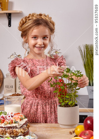 Little girl is making a homemade cake with an easy recipe at kitchen against a white wall with shelves on it. 95837689
