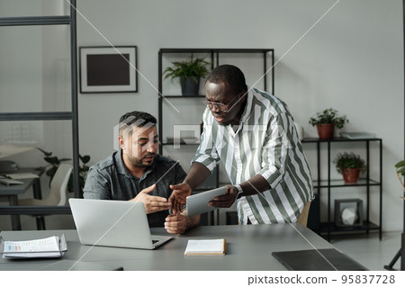 Two young multicultural colleagues with mobile gadgets arguing about data Two young multicultural colleagues with mobile gadgets arguing about data 95837728